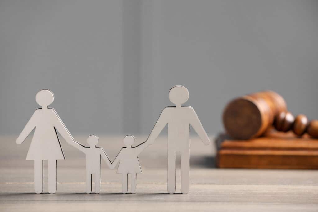 Paper figures of parents with children and gavel on wooden table