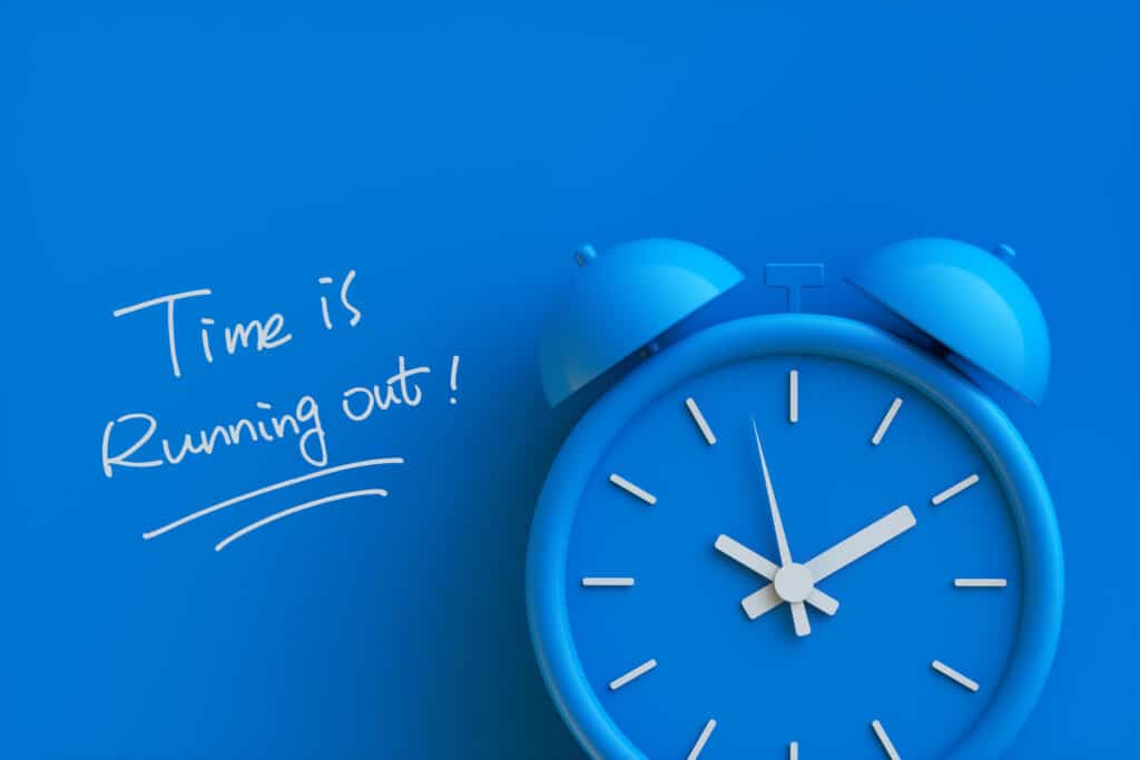 Blue alarm clock on a blue background with the handwritten text 'Time is running out!'